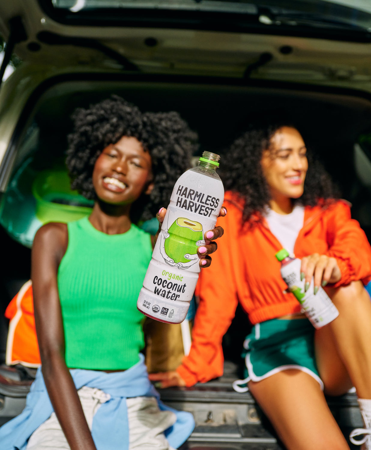 Two people drinking Harmless Harvest Organic Coconut Water in the back of a car.