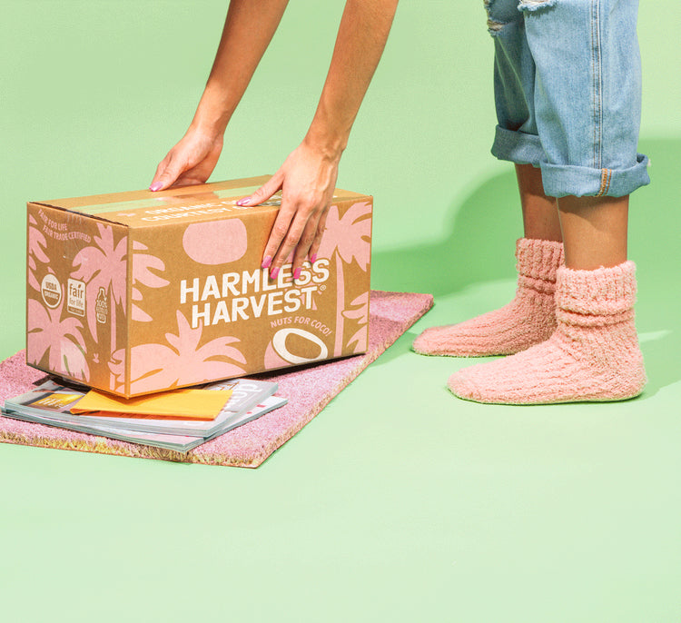 Person with pink socks reaching for box of Harmless Harvest Organic Coconut Water on doormat