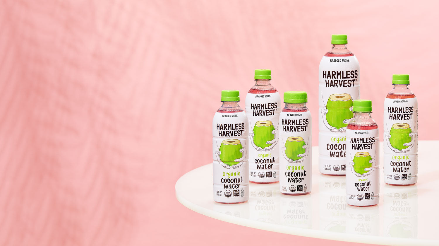 Harmless Harvest Organic Coconut Waters on white table with pink background.