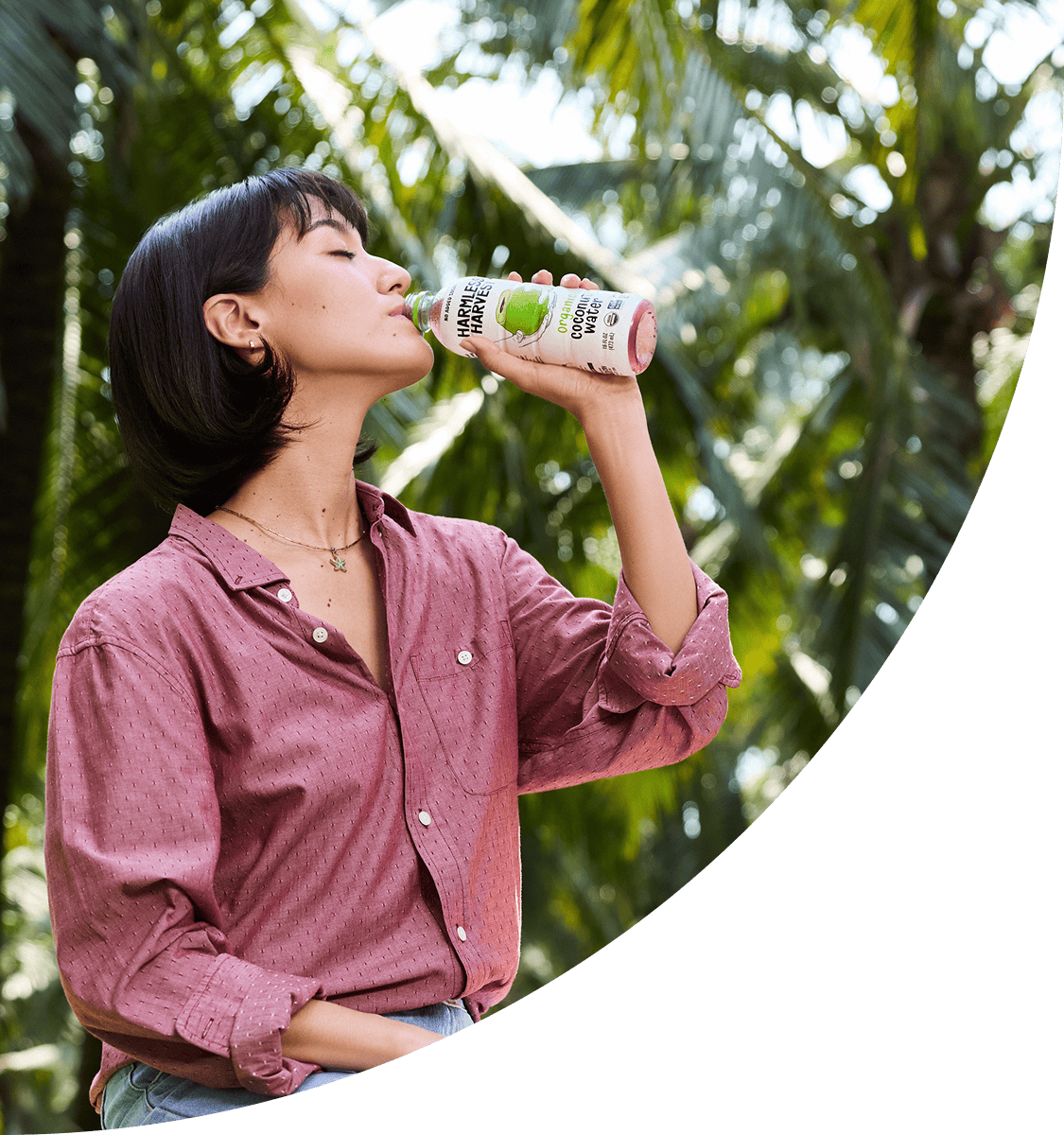 Woman drinking from a Harmless Harvest bottle in a coconut grove