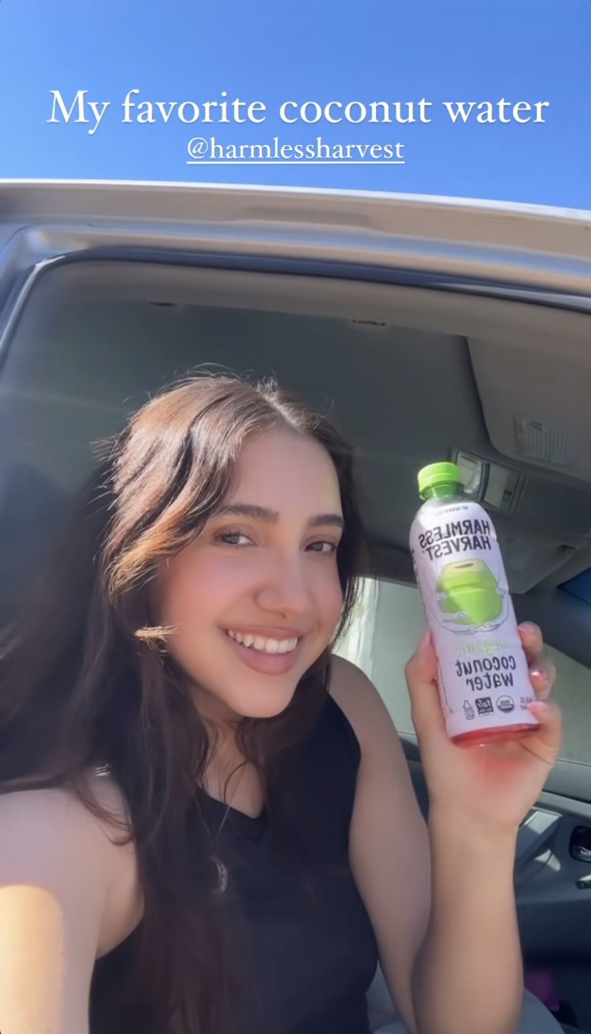 Woman in car holding Harmless Harvest Organic Coconut Water. Caption: My favorite coconut water @harmlessharvest.